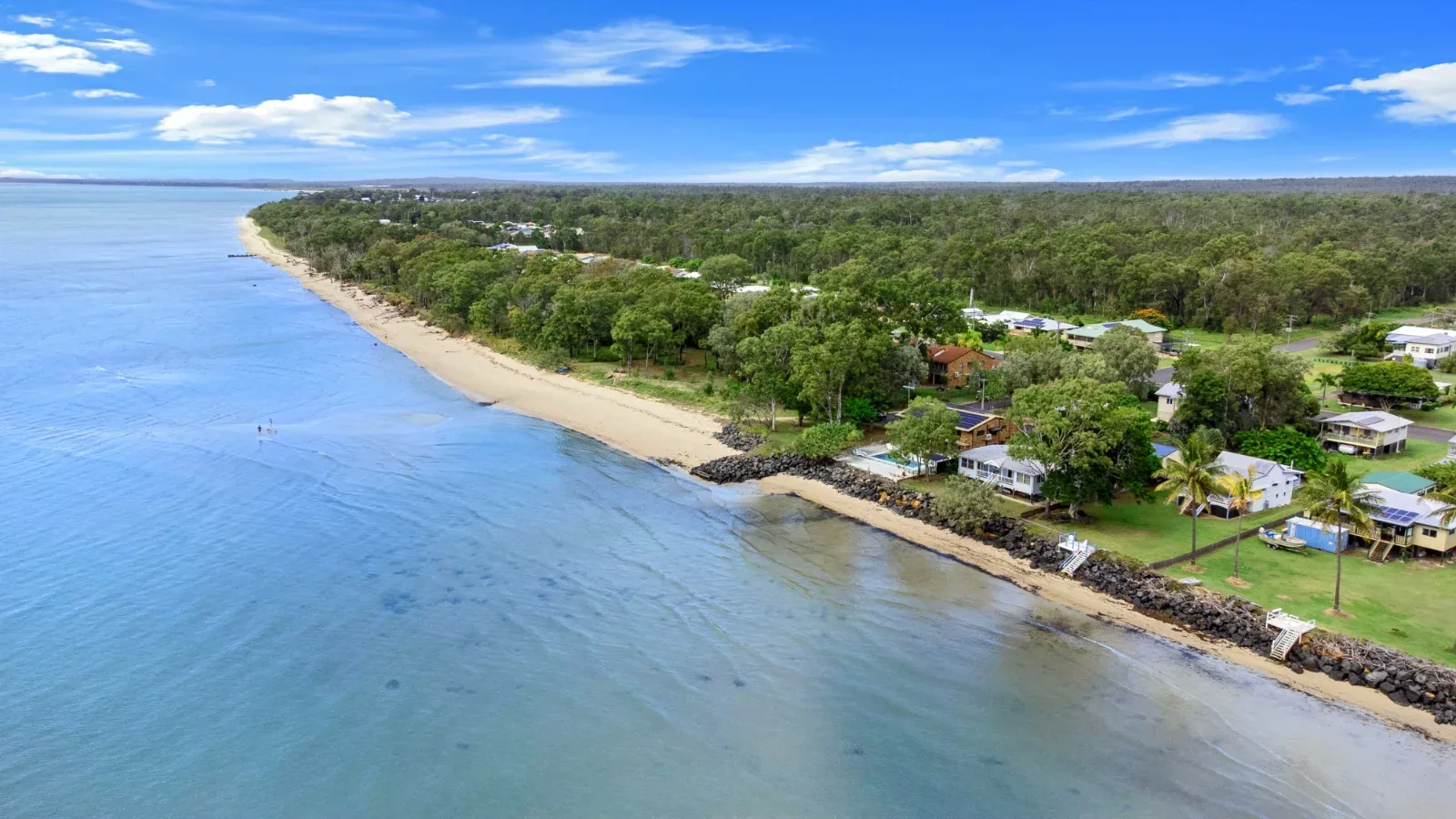 The tree-lined Burrum Heads foreshore stretching beside calm coastal water