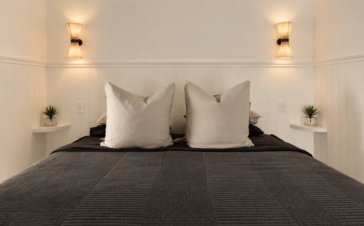 Sunset Waters bedroom with dark bedding and warm bedside wall lights