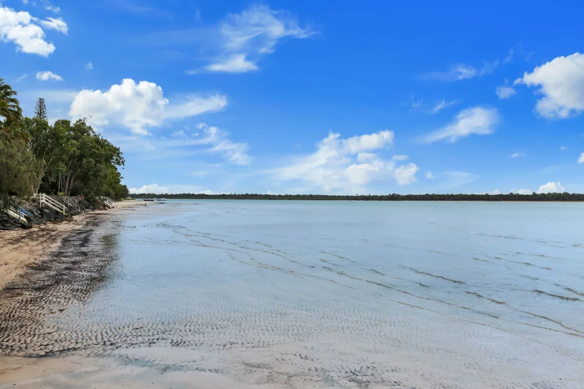 The calm Burrum Heads shoreline, with sand, shallow water and trees beside the beach
